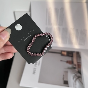 Detail showing pink rhinestone hair clip on black card held against lifestyle background