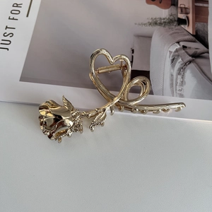 Detail of a golden metal hair claw clip featuring a realistic rose and heart outline design