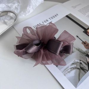 Détail d'une pince à cheveux avec nœud en organza corail et ruban à bord doré