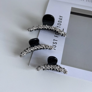 Dettaglio di tre mollette nere per capelli con strass scintillanti su sfondo rivista