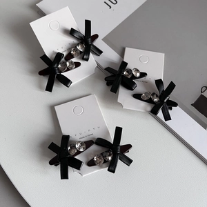 Three pairs of black leather bow hair clips with crystal rhinestones on a display card