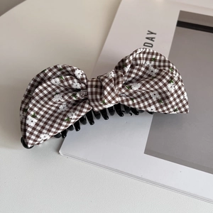 Detail of a plaid bow banana hair clip with embroidered white flowers and sturdy black grip
