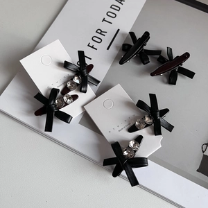 Elegant black leather bow hair clips with rhinestones on a white display card
