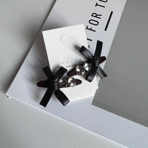 Detail of two black faux leather bow hair clips with crystal rhinestones on a display card