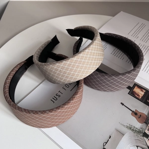 Close-up of three wide plaid fabric headbands in beige and grey on a white magazine