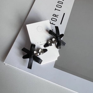 Close-up of black leather bow hair clips with rhinestones on minimalist white packaging
