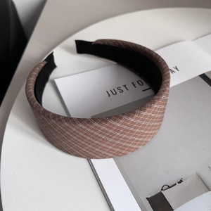Detail of a brown plaid wide headband with textured fabric on a minimalist white desk