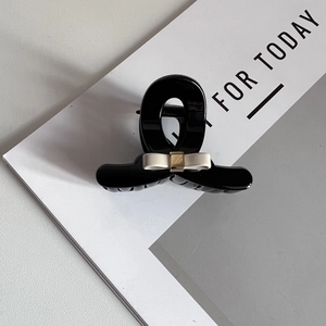 Detailed close-up of a black resin hair claw clip with an elegant beige silk bow decoration