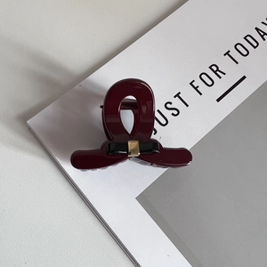 Detail of burgundy hair claw clip featuring a black bow and gold metal centerpiece