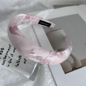 Close-up of pink satin headband with purple floral embroidery and padded sponge texture