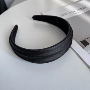 Macro shot of the black wide fabric headband with detailed pleated texture on white surface