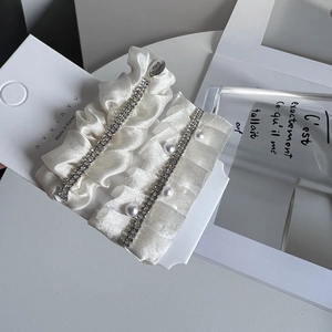 Close-up of white satin pleated hair clips with crystals and pearls on brand card