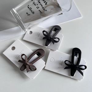 Three elegant fabric bow hair clips in black and dark brown on a white display card