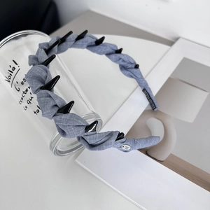 Detail of blue textured fabric headband featuring shark teeth studs and handmade label