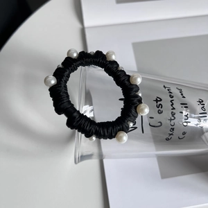 Détail d'un chouchou noir en soie avec perles blanches élégantes sur un support en verre