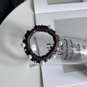 Détail d'un chouchou marron foncé orné de perles blanches sur un fond minimaliste épuré