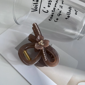 Detail of a brown bow hair claw clip with white pearls, flower, and crystal accents