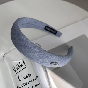 Detail of blue fabric headband featuring handmade tag and small rhinestone metal emblem