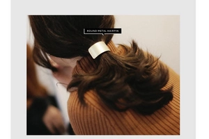 Golden matte curved metal hairpin styled on a woman's low ponytail with warm lighting