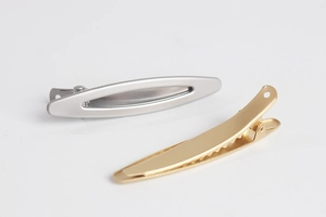 Detailed view of minimalist matte gold and silver metal duckbill hair clips on white background