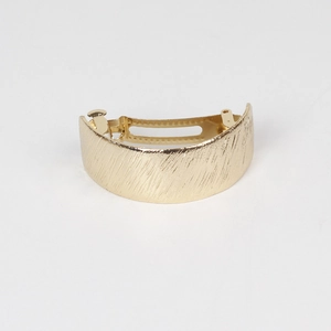 Macro detail of golden metal barrette with vertical brushed texture and curved design
