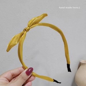 Détail d'un serre-tête en satin jaune avec un nœud artisanal et embouts noirs