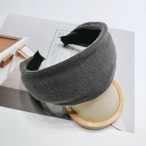 Close-up of deep grey ribbed knit wide headband on a minimalist wooden display stand