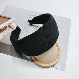 Detail shot of black wide-brimmed headband with vertical ribbed texture on a base