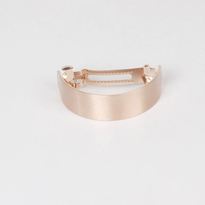 Detail view of rose gold curved metal hair clip with a brushed texture and spring mechanism