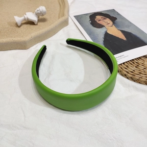 Gros plan sur un serre-tête large en cuir vert litchi sur fond artistique vintage