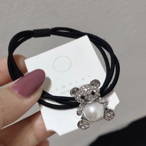 Dettaglio di un elastico per capelli nero con un ciondolo a forma di orso e perla
