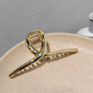 Détail de la pince à cheveux minimaliste en alliage doré au design de boucle croisée