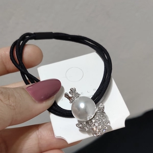 Dettaglio di un elastico nero per capelli con ciondolo a perla e corona lucida