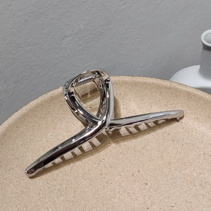 Détail d'une pince à cheveux argentée en métal au design torsadé sur un plateau chic