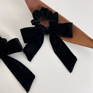 Detail of elegant black velvet hair scrunchie with long ribbon bow on warm white surface