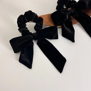 Detailed view of black velvet bow hair ties with elegant long ribbons on a wooden tray