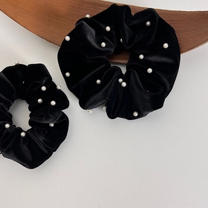 Chouchous élégants en velours noir avec perles blanches posés sur un plateau en bois