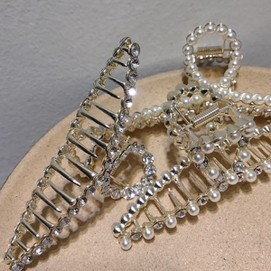 Elegant gold metal hair claw clips with rhinestones and pearls on a beige tray
