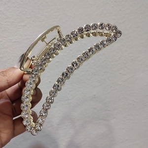 Détail d'une grande pince à cheveux dorée ornée de strass tenue à la main