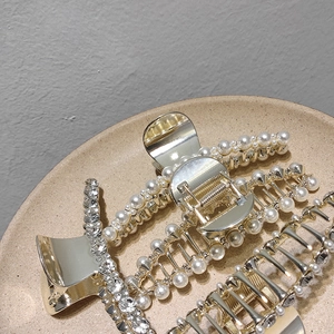 Détail de pinces à cheveux dorées avec perles et strass posées sur un plateau en céramique