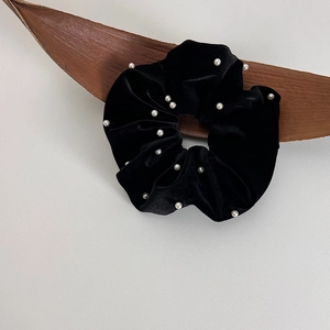 Gros plan d'un chouchou en velours noir orné de perles blanches élégantes sur fond minimaliste