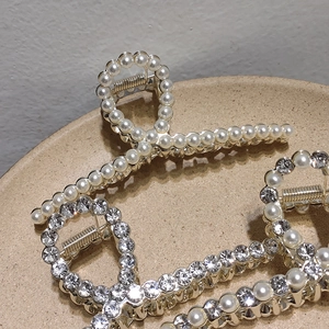 Elegant large metal hair claws with pearls and rhinestones on a ceramic display