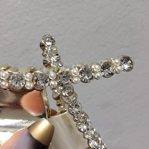 Détail d'une pince à cheveux en métal doré ornée de perles blanches et strass brillants