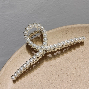 Macro detail of large gold metal hair claw clip with cross design and white pearls inlay