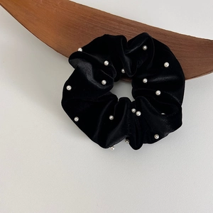 Détail d'un chouchou en velours noir avec perles blanches sur fond en bois minimaliste