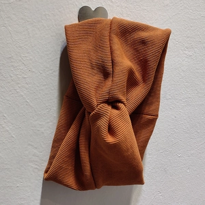 Gros plan du bandeau tricoté caramel avec nœud suspendu sur un mur blanc texturé