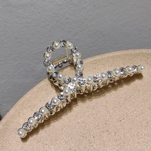 Detail view of a gold hair claw clip with crossed pearls and sparkling rhinestones