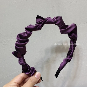 Detail of purple satin headband featuring elegant pleated folds and twisted knot design
