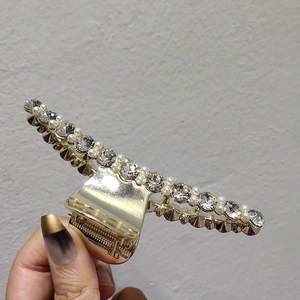 Détail de la pince à cheveux dorée ornée de strass brillants et de perles blanches