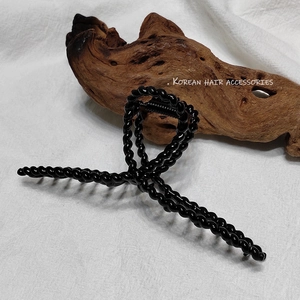 Détail d'une grande pince à cheveux noire tressée posée sur du bois et du tissu